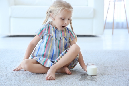 Girl sitting on carpet by milk spill
